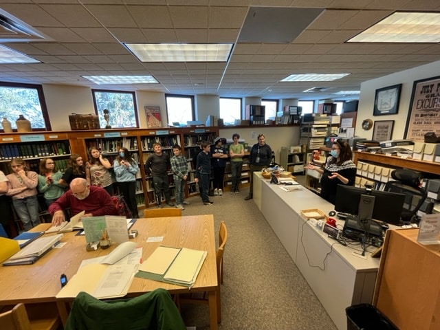 History Room archivist gives a tour to fifth graders while a researcher studies materials at the work table.